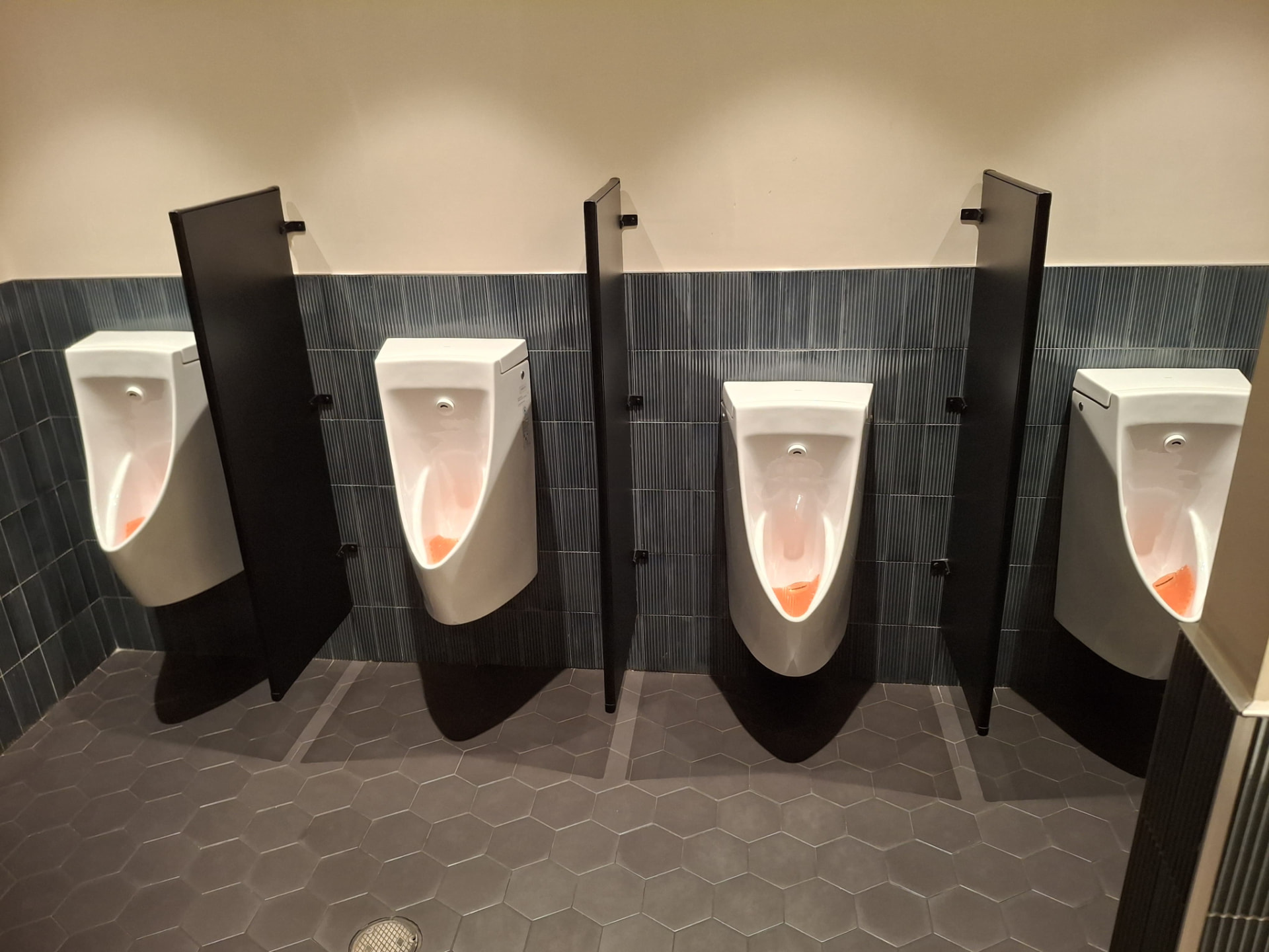 Row of four urinals with black privacy dividers, freshly sanitized tile walls and floor — Ledian's Cleaning Services