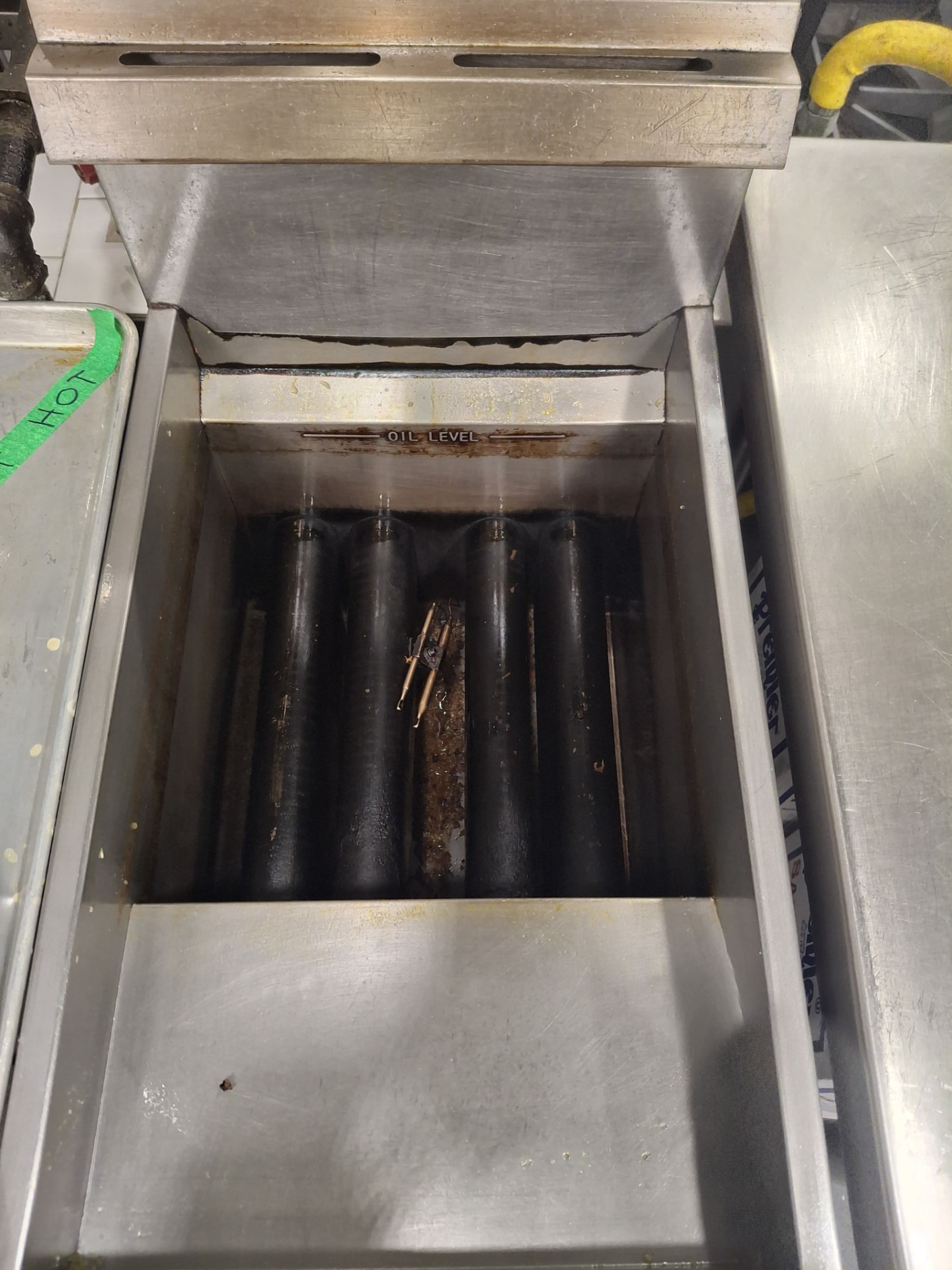 Commercial deep fryer well caked with blackened oil and food debris before cleaning by Ledian's Cleaning Services